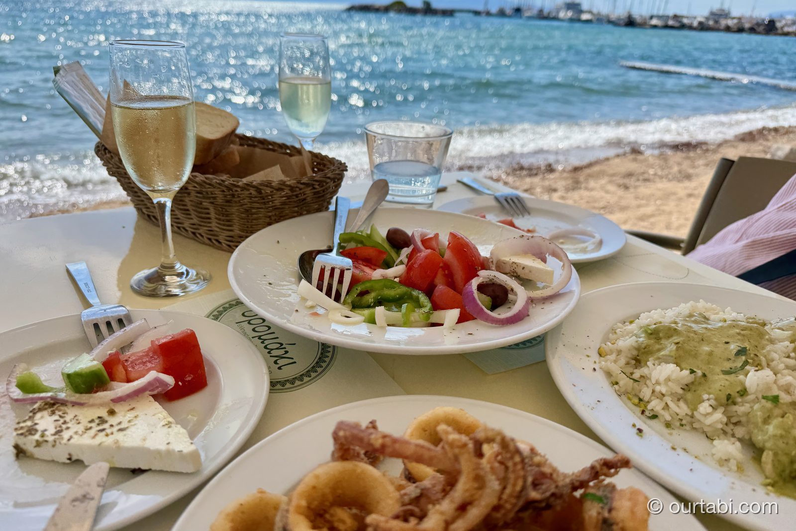 海辺のテーブルに並んだギリシャ料理とワイン