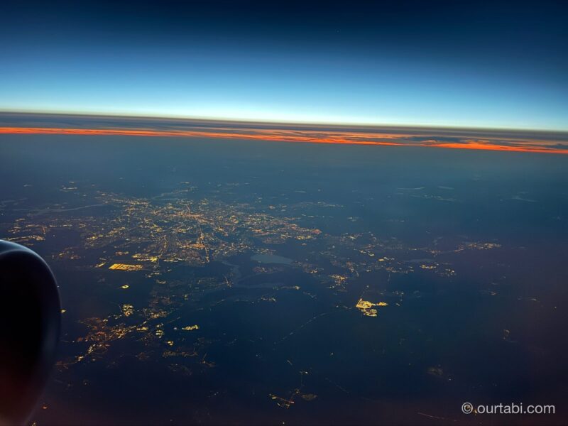 夜のフライトの機窓から見た、地平線の夕焼けと地上の街明かり