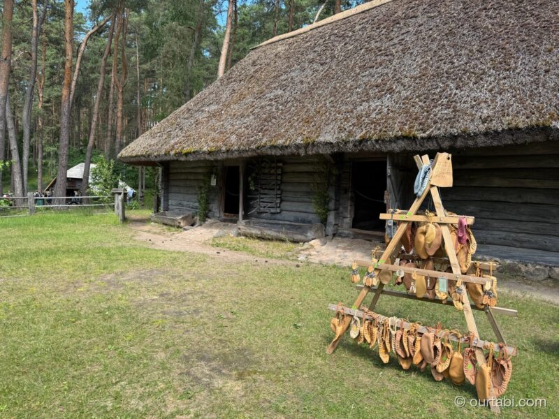 茅葺き屋根の家の前に置かれた木の台に、革製の履き物が吊るされている