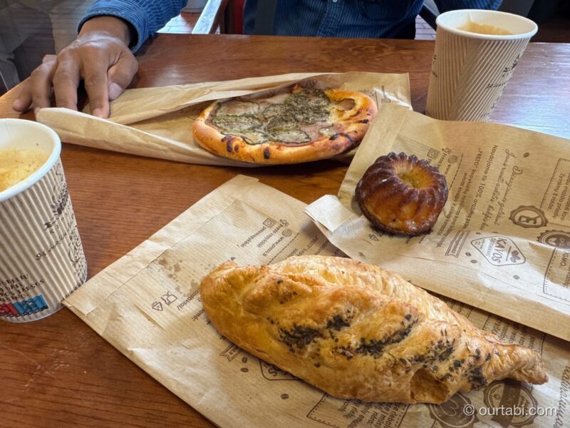 紙の上に置かれたピザ、焼き菓子、包み焼きのパンとコーヒー