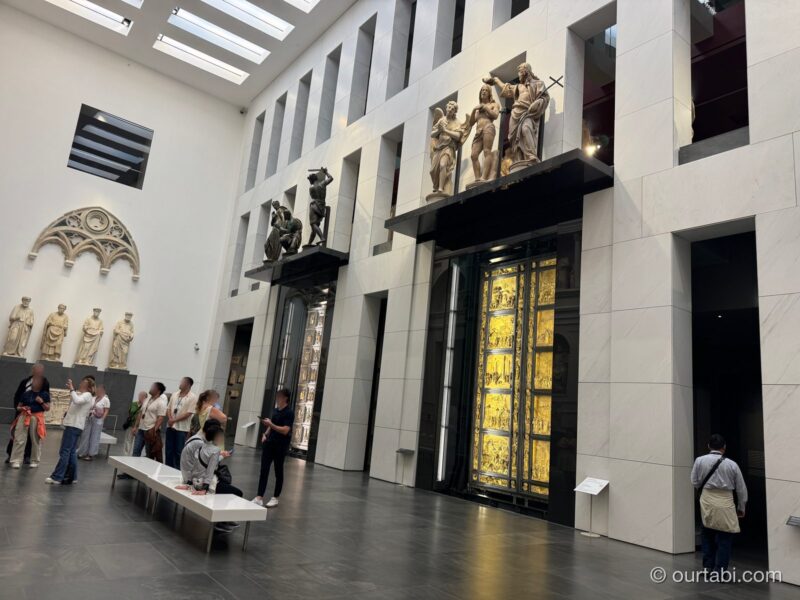 博物館の吹き抜けの大広間。右に金色の扉と、上に彫刻が並ぶ