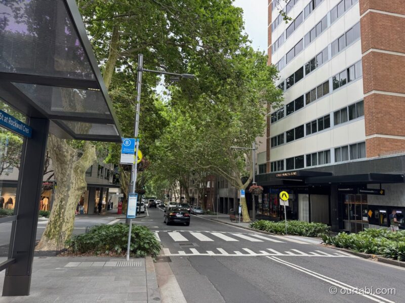 Macleay Streetのバス停の屋根と街路樹の通り